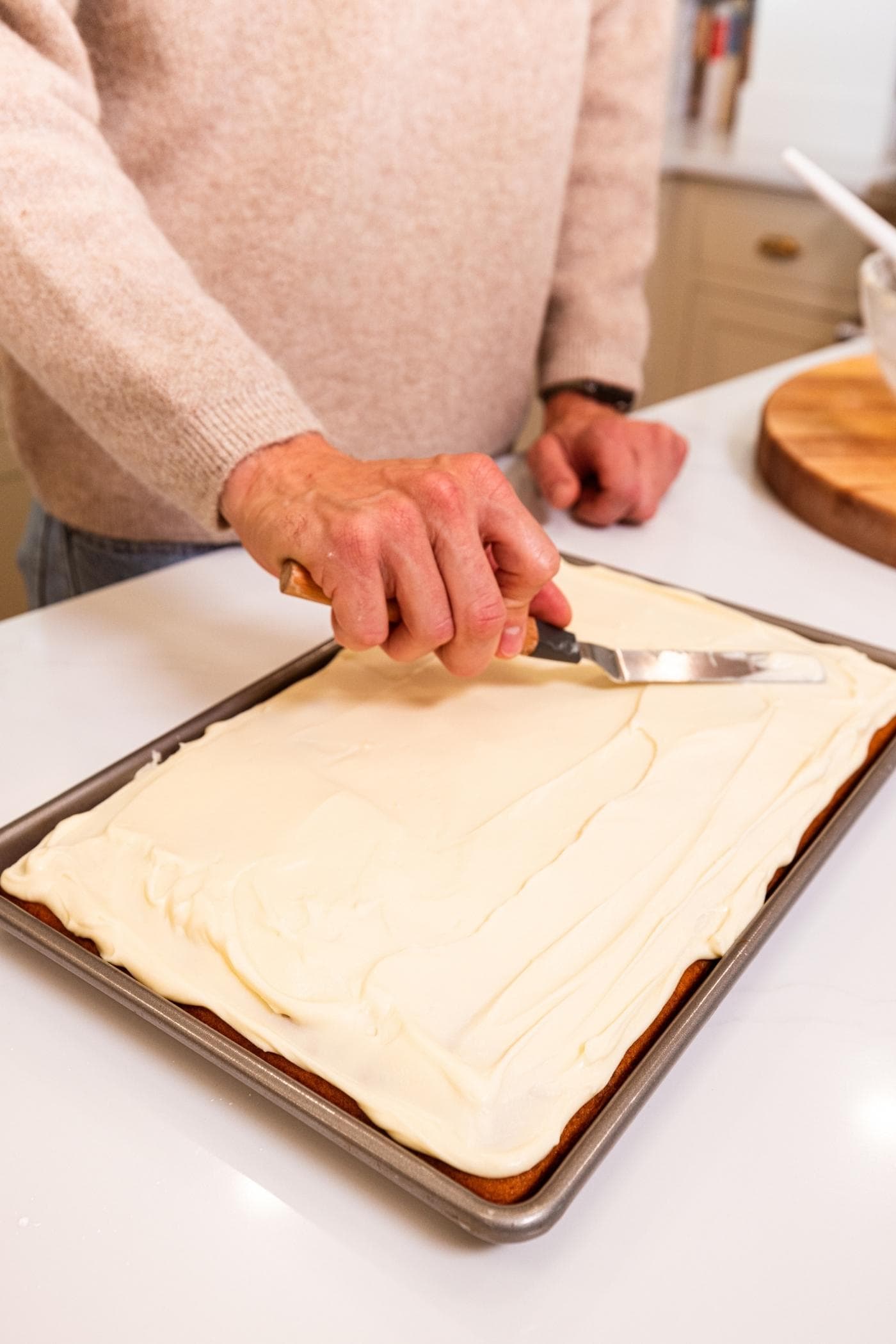 Hand holding offset spatula smoothing cream cheese frosting over the top of pumpkin bars.