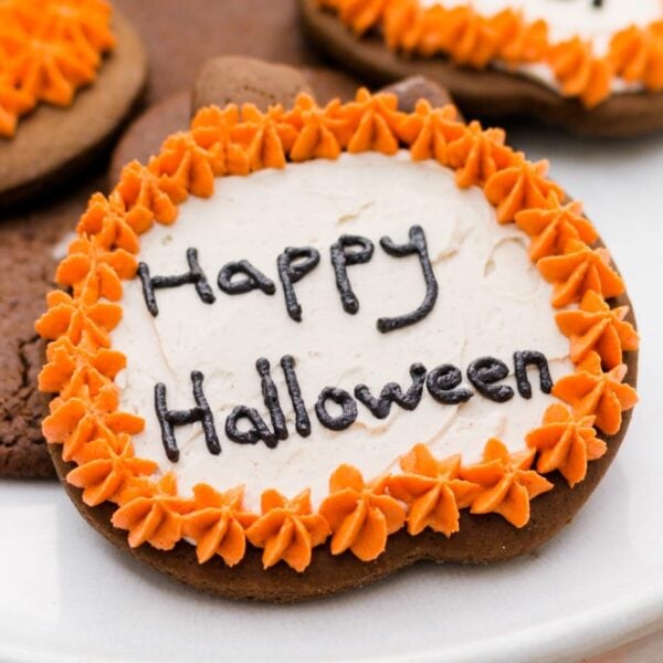 Spiced ginger cutout cookies topped with orange and white frosting sitting on white cake plate