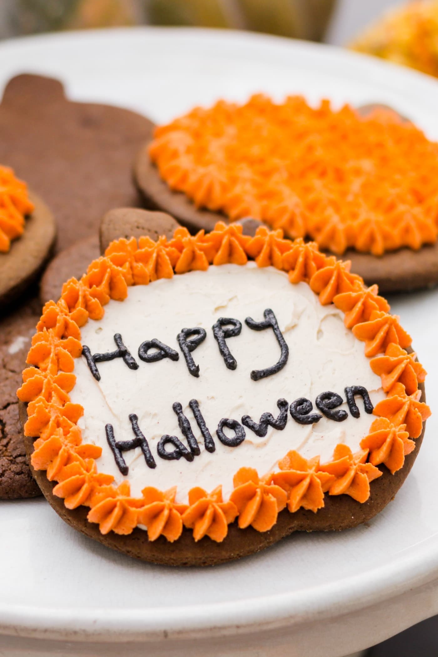 Spiced ginger cutout cookies topped with orange and white frosting sitting on white cake plate