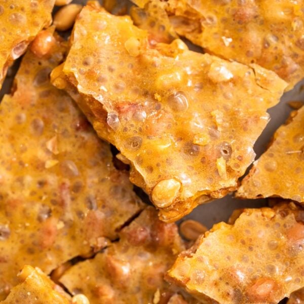 Top down view of yellow colored pieces of peanut brittle dotted with peanuts sitting on baking tray