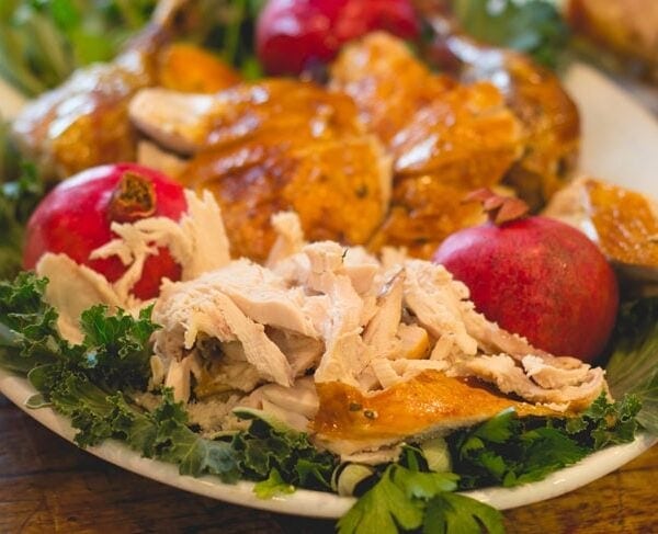 Plate with lettuce underneath a pile of carved turkey meat with pomegranate on plate as well.