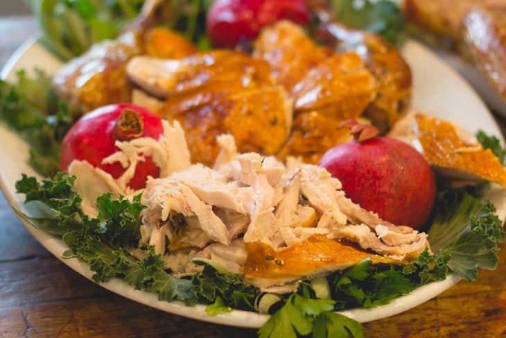 Plate with lettuce underneath a pile of carved turkey meat with pomegranate on plate as well.