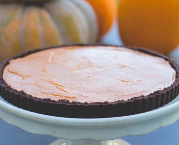 Round cake plate with pumpkin tart with chocolate crust on top with pumpkins in background.