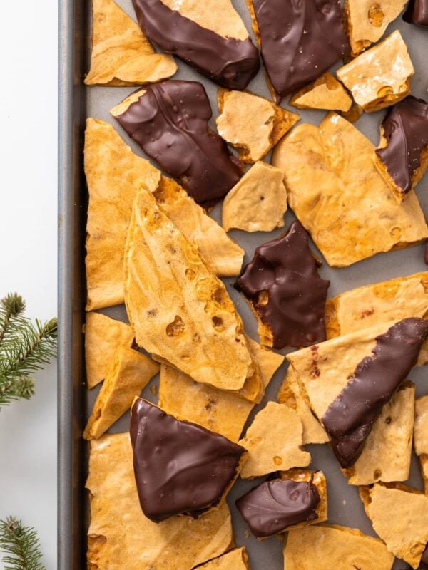 Top down view of baking pan filled with pieces of yellow candy, some with dark chocolate on top and other plain all on white colored countertop