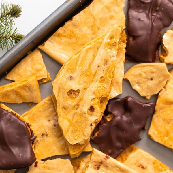 Top down view of oddly shaped pieces of yellow-colored candy sitting on baking pan, some with chocolate on top all on white countertop surface