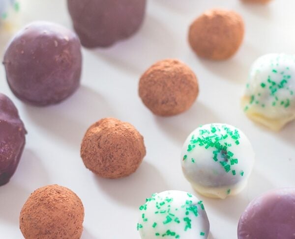 Three different types of decadent truffles sitting on white surface with rows of chocolate lined up