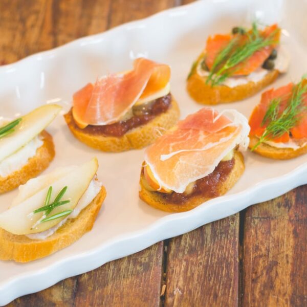 Three different types of crostini sitting on white serving platter with wooden surface underneath