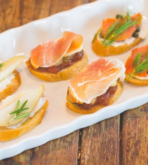Three different types of crostini sitting on white serving platter with wooden surface underneath