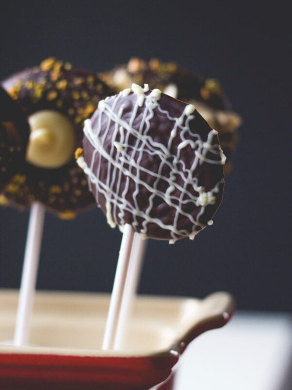 A few chocolate pops sitting in red colored container with black background with white chocolate drizzled over the top