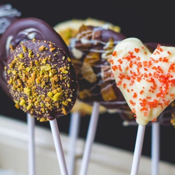 Lots of chocolate pops made from different types of chocolate topped with various different toppings including nuts and sprinkles