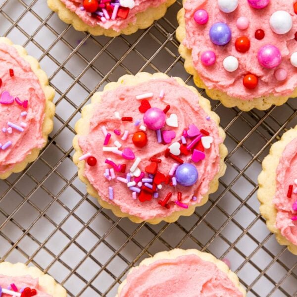 Top down view of baking rack filled with sugar cookies with pink frosting and sprinkles on top