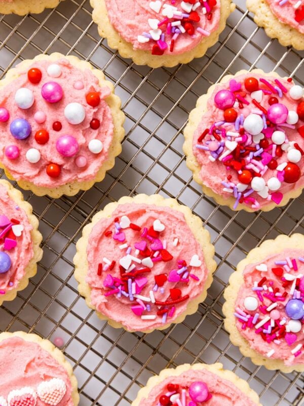 Top down view of cooling rack with sugar cookies with frosting and sprinkles all over the top in shades of pink and red
