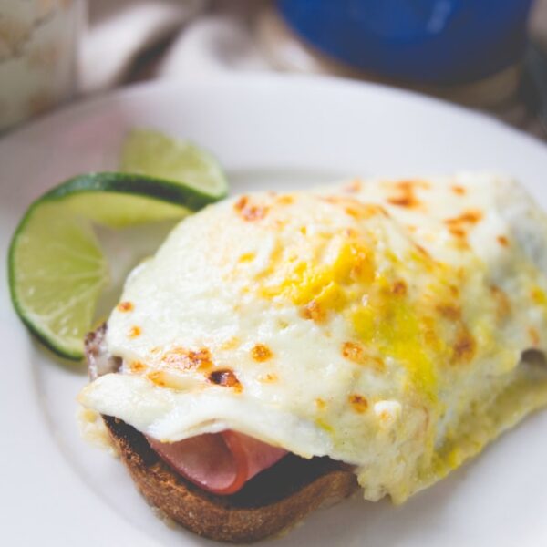 White plate with open-faced sandwich topped with fried egg with lime wedge in background