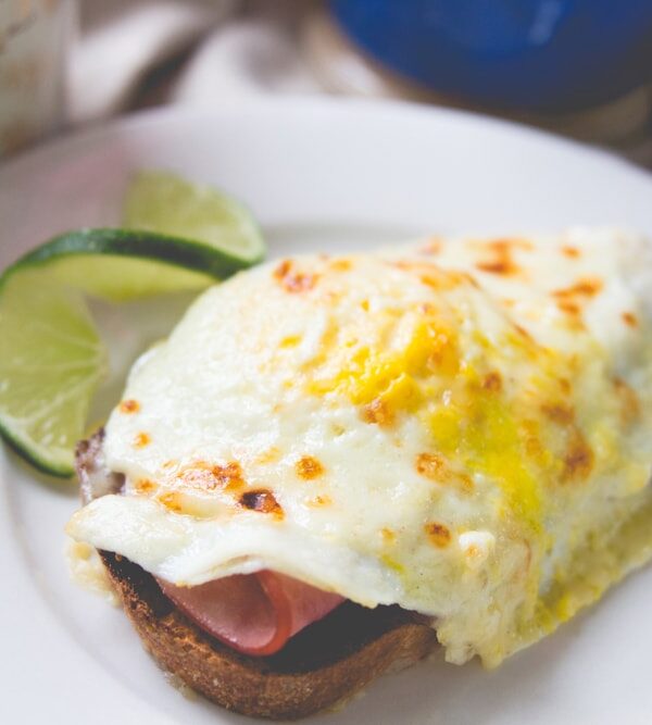 White plate with open-faced sandwich topped with fried egg with lime wedge in background
