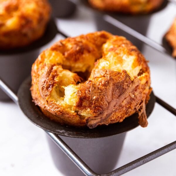 Popped and golden brown popovers sitting in black popover pan after coming out of the oven.
