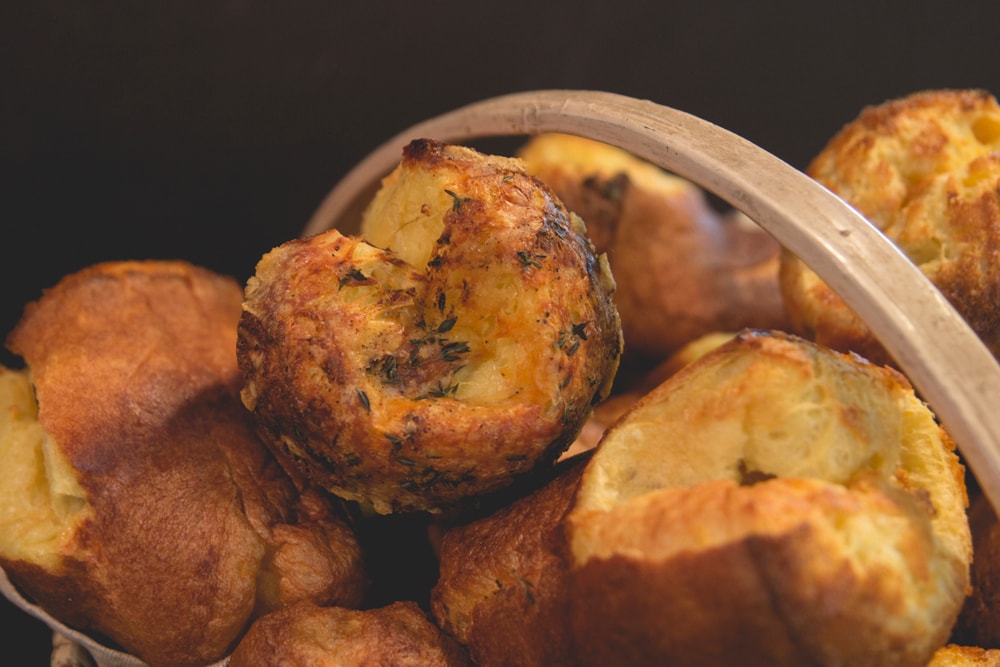 Popovers piled on top of each other in a wood basket with some sprinkled with herbs all in front of a black background