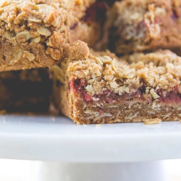 Stacks of rhubarb crumb bars sitting on white plate showing the middle jam layer of the bars