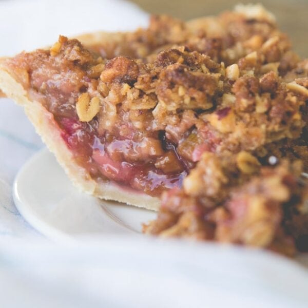 Side view of slice of rhubarb pie sitting on white plate with napkin behind