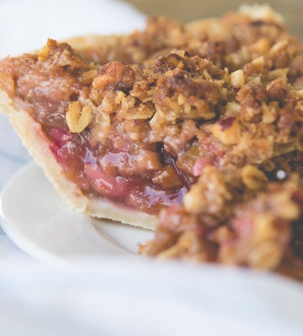 Side view of slice of rhubarb pie sitting on white plate with napkin behind