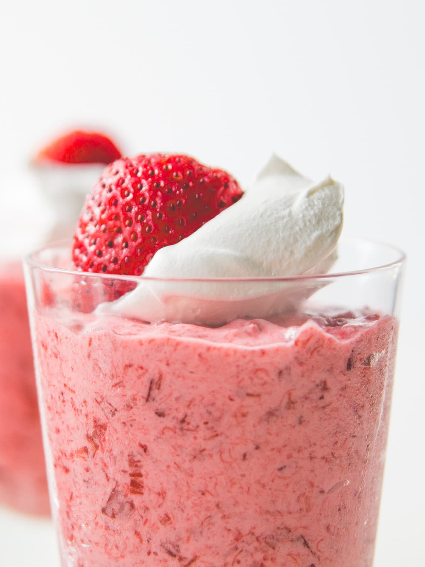 Large glass filled with pink strawberry and rhubarb fool topped with whipped cream and strawberry.