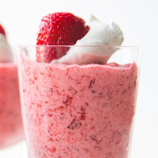 Glass filled with strawberry rhubarb fool topped with whipped cream and a bright red strawberry.