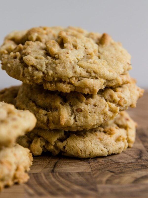 Stack of three light brown crunchy peanut cookies sitting on a wood cutting board