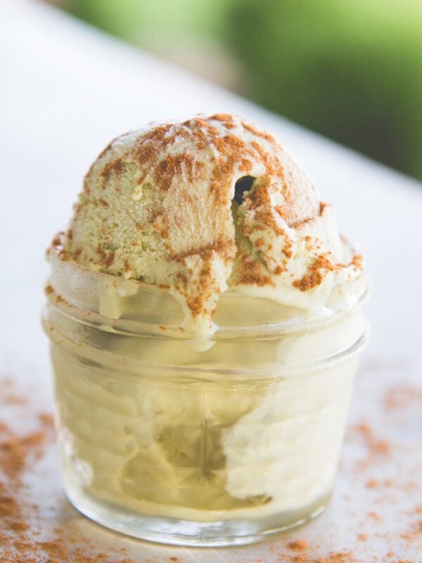 Small glass container filled with green colored matcha green tea ice cream with cinnamon sprinkled over the top sitting on surface outside