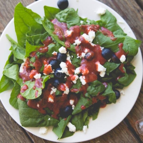 White plate filled with lettuce and topped with blueberries, feta cheese, and strawberry vinaigrette dressing all on wood surface