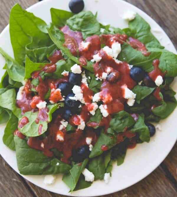 White plate filled with lettuce and topped with blueberries, feta cheese, and strawberry vinaigrette dressing all on wood surface