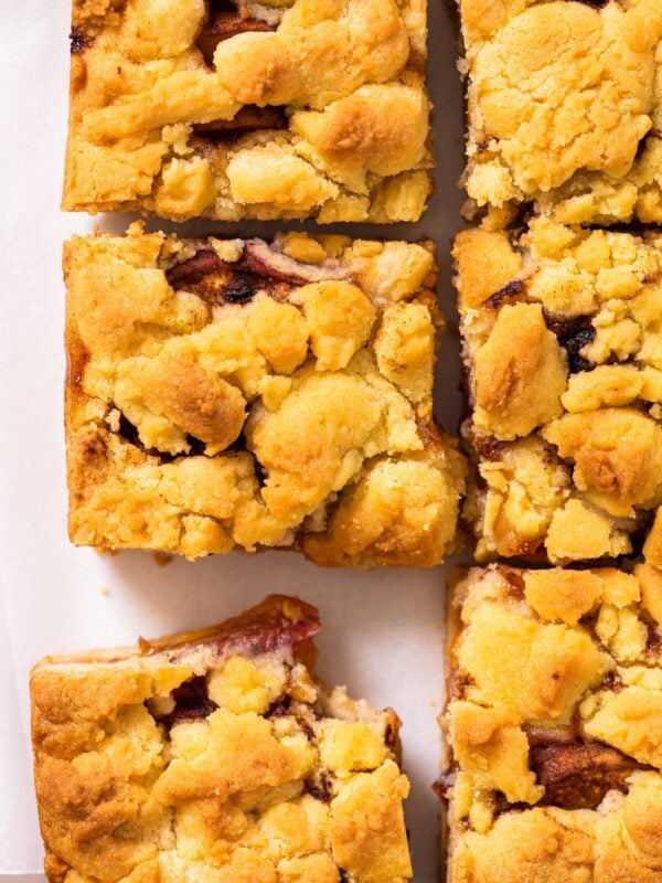 Top down view of squares of peach crumb bars sitting on white countertop with slices of peaches on cutting board