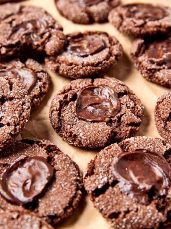 Pile of chocolate mint cookies with crackly edges sitting on piece of parchment with mint on top.