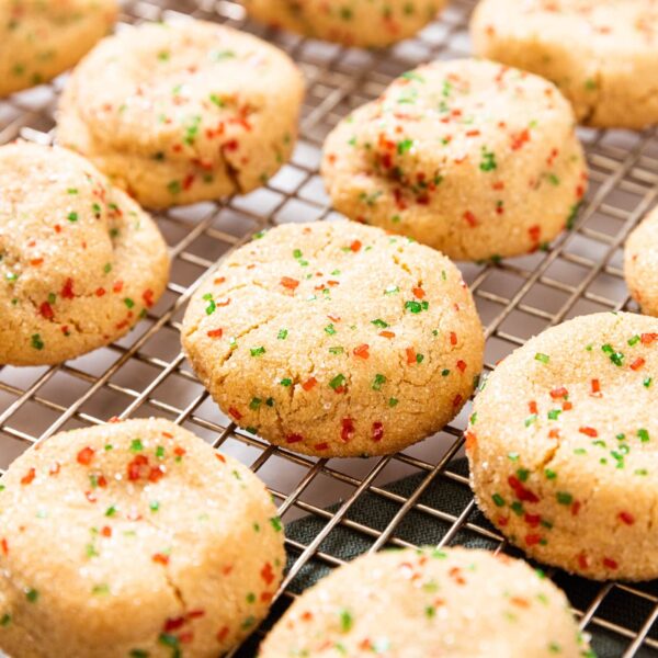 Yellow colored candy bar cookies with red and green sprinkles embedded on top sitting on wire cooling rack.