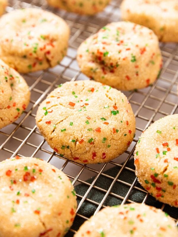 Lightly golden brown candy bar cookies with red and green sanding sugar embedded in dough sitting on wire cooling rack after coming out of the oven.