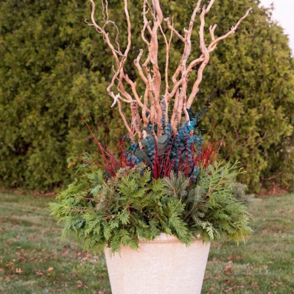 Large concrete urn with greenery around the base with red twigs, eucalyptus, and large branches coming out of the top.