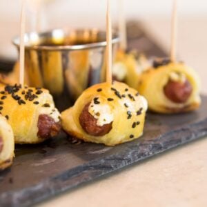 Little smoky hot dogs wrapped in dough and sprinkled with sesame seeds all on slate serving platter on marble surface