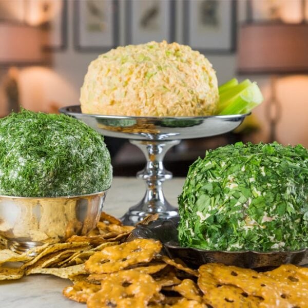 Three silver platters filled with cheese balls sitting on marble surface with pretzels and crackers all around