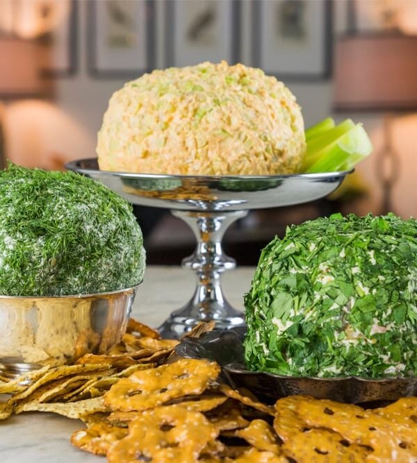 Three silver platters filled with cheese balls sitting on marble surface with pretzels and crackers all around