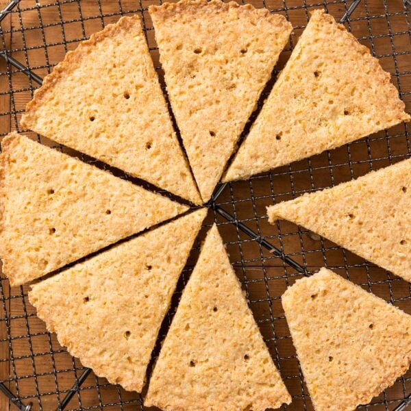 Top down view of triangle-shaped lemon shortbread cookies sitting on wire cooling rack all on wood surface