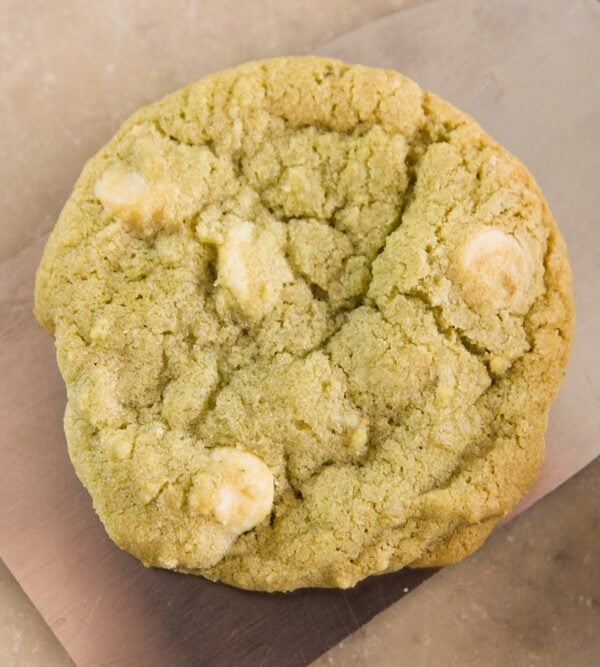 Light green colored matcha green tea cookie sitting on metal spatula on marble surface with white chocolate pieces in cookie