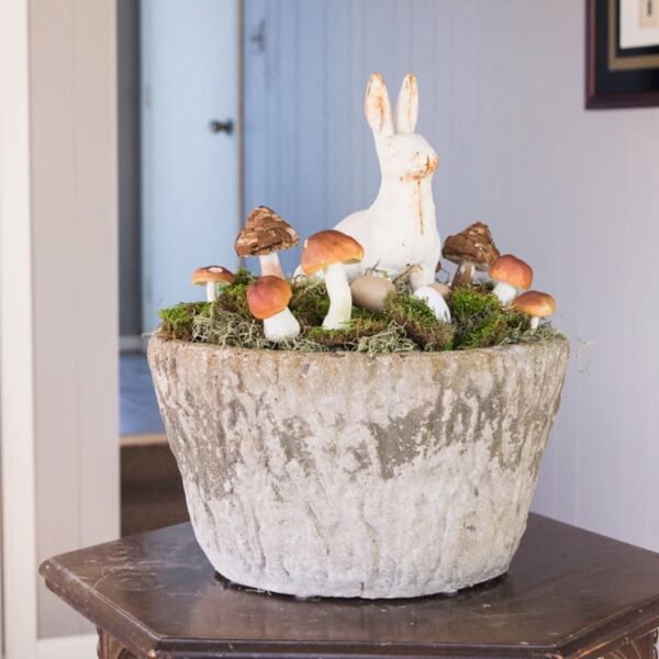 Concrete large vessel sitting on a wooden table decorated with cast iron bunny and small mushrooms for an Easter display.
