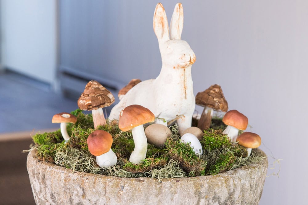 Concrete bowl filled with moss and mushrooms and topped with a cast iron white bunny for an Easter display on a table.