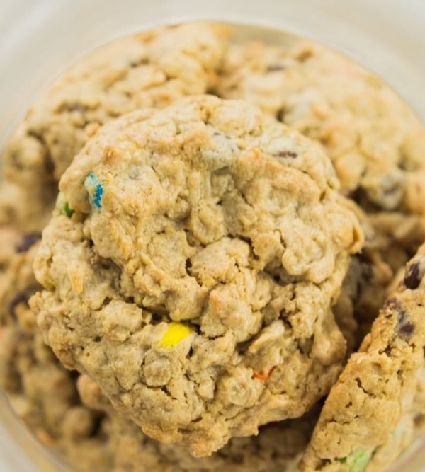 Top down view of glass cookie jar filled with lots of monster cookies with M&M's showing through the oats