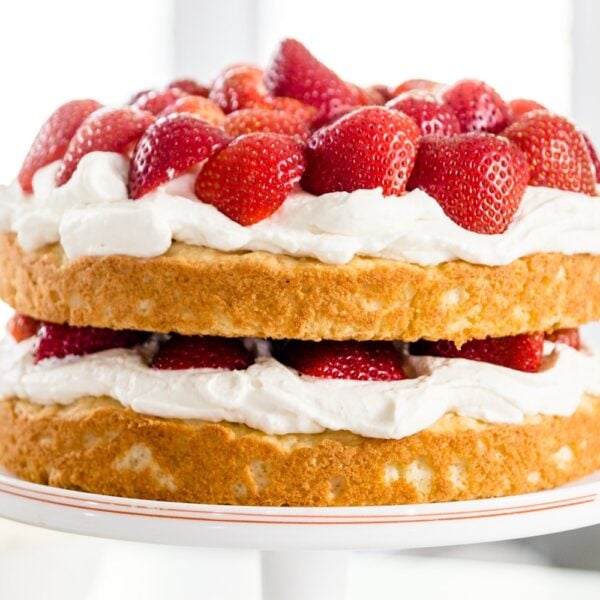 Strawberries, whipped cream and yellow cake in two layers on a white cake plate