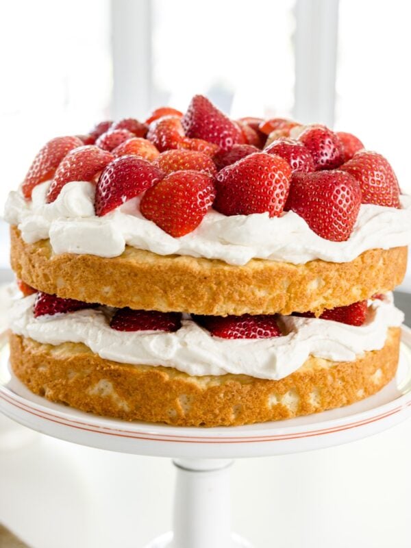 Strawberries, whipped cream and yellow cake in two layers on a white cake plate
