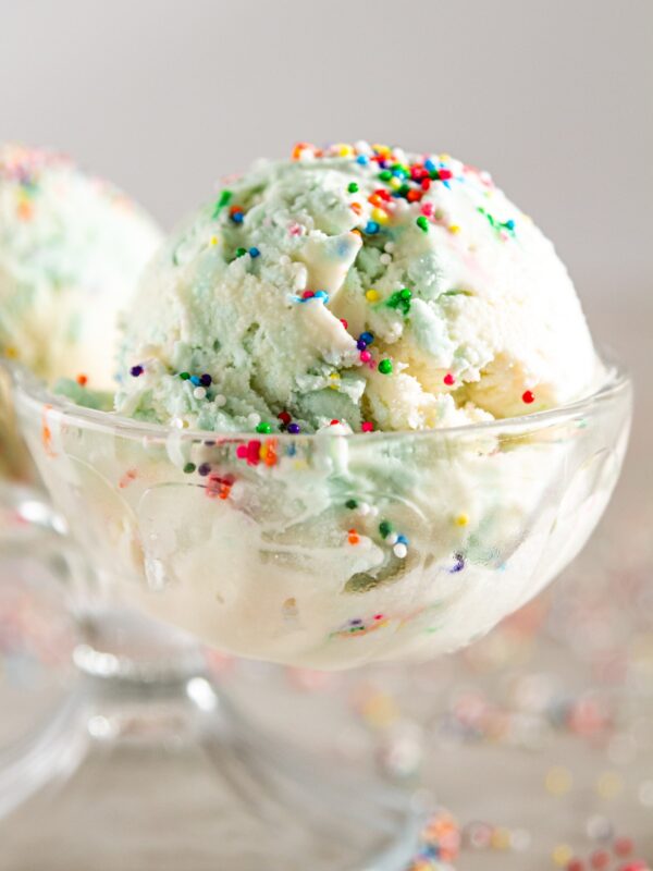 Double sided bowl filled with scoop of birthday cake ice cream with sprinkles on top.
