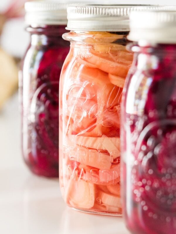Three canned beet recipes in Ball canning jars on a white surface with golden beet in background.