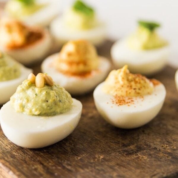 Three types of deviled eggs sitting on wood board, some eggs with paprika and others with pine nuts