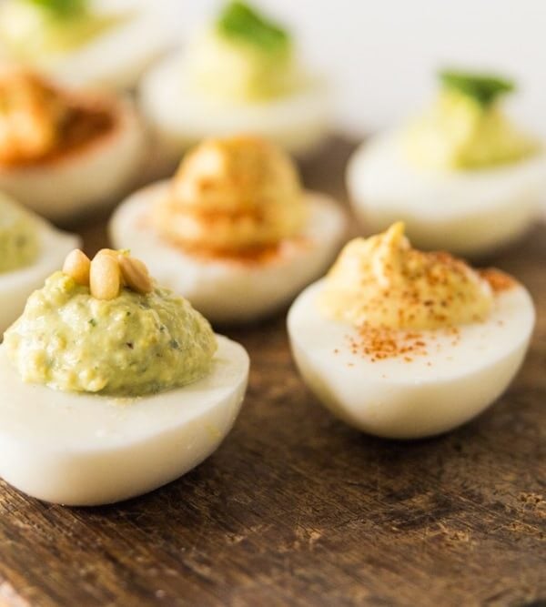 Three types of deviled eggs sitting on wood board, some eggs with paprika and others with pine nuts