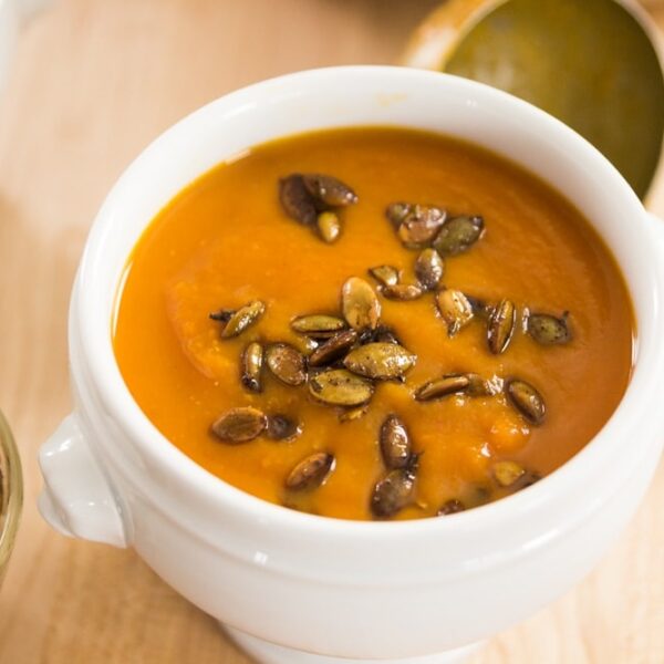White bowl filled with orange colored chipotle squash soup with roasted pepitas on top all on light wood surface