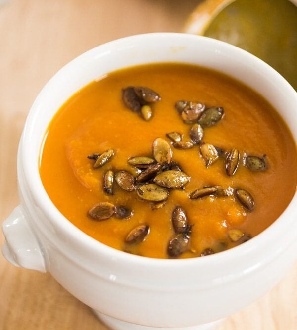 White bowl filled with orange colored chipotle squash soup with roasted pepitas on top all on light wood surface